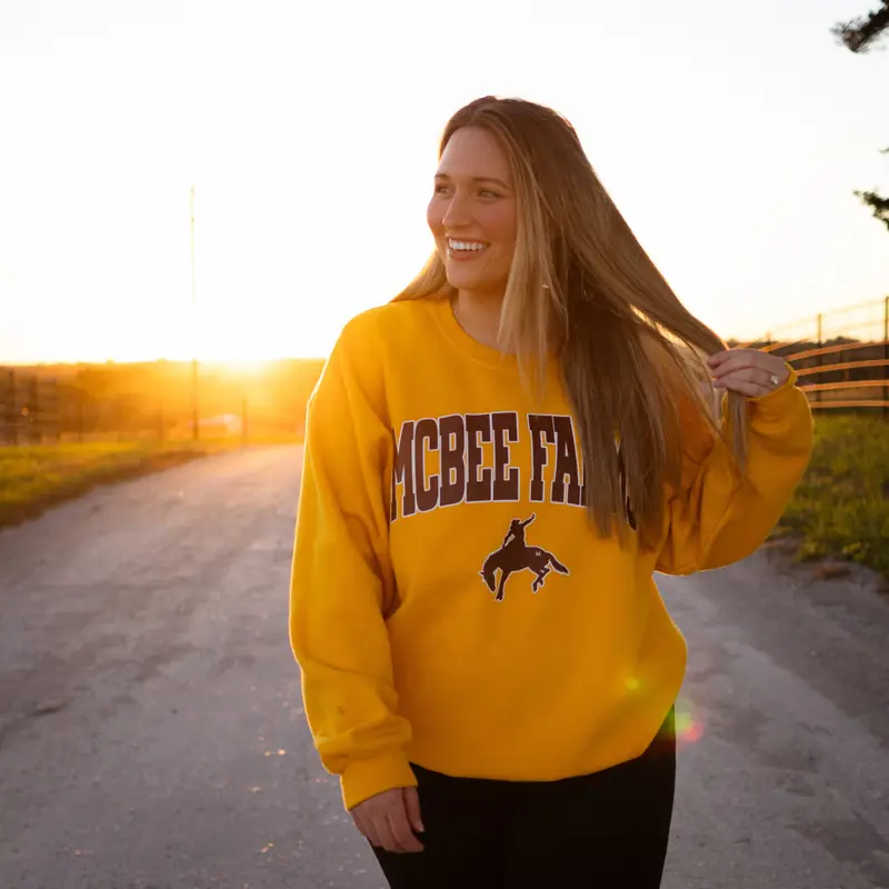 Kacie laughing on a gravel farm road at sunset in a McBee Farms sweatshirt